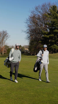 Two golfers walking on a golf course with clubs and bags.