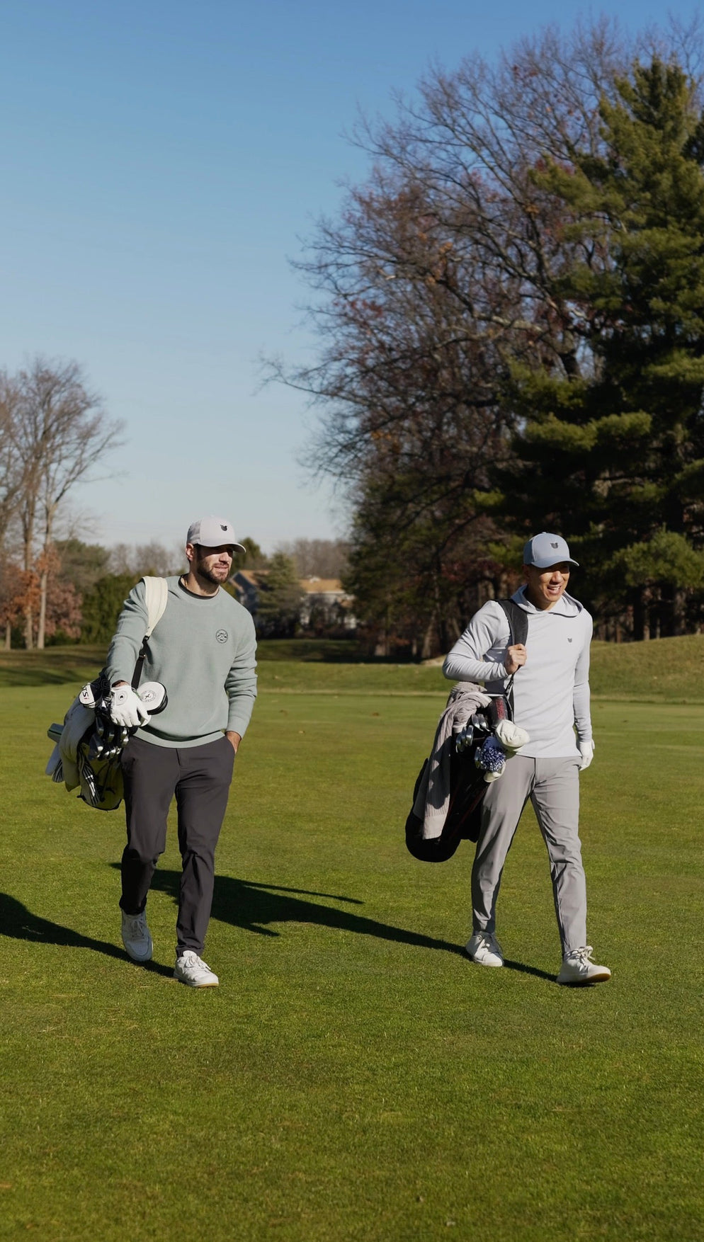 Two golfers walking on a golf course with clubs and bags.